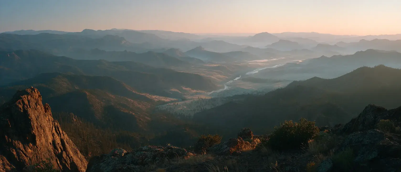 A high ridge overlooking a wide valley and a winding river at dawn